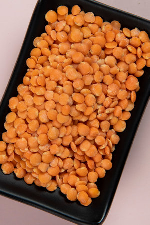 Red lentils in black bowl on pink background. Topview.の写真素材