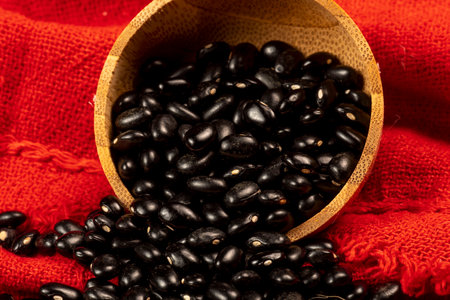Black beans in a wooden bowl on a red background. Selective focus.の写真素材