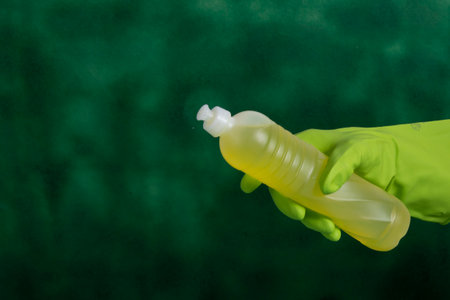 Hand with protective glove holding packaging of cleaning products used for home hygiene in a green backgroundの写真素材