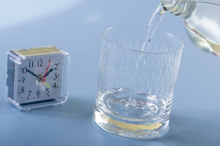 Detail of the person filling the glass with water. Concept of reminding hydration time on blue backgroundの写真素材