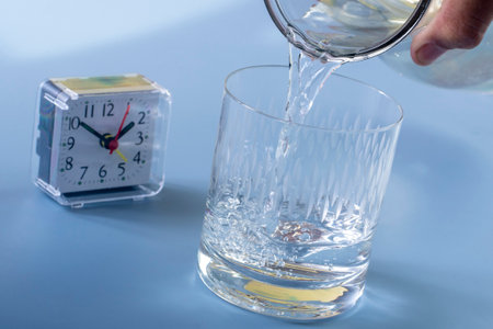 Alarm clock and a glass of water on a blue background.の写真素材