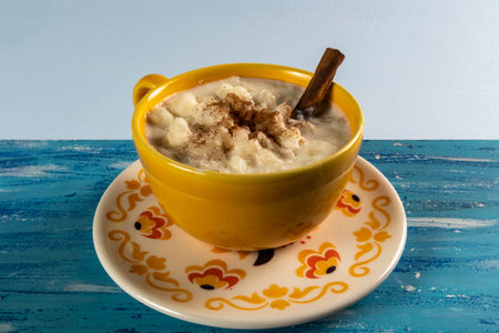 Typical Brazilian sweet dessert, Canjica. White corn porridge with cinnamon and coconut. Consumed at June festivals (festa Junina) on a rustic blue tableの写真素材