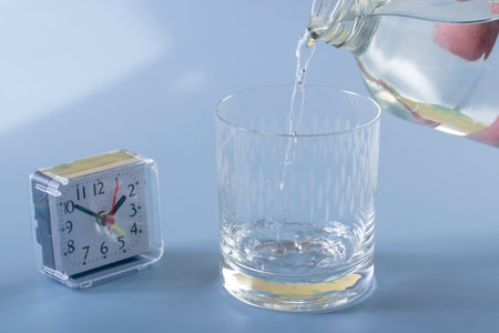 Detail of the person filling the glass with water. Concept of reminding hydration time on blue backgroundの写真素材