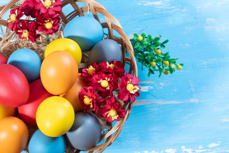 Easter eggs in a basket with flowers on a blue wooden backgroundの写真素材