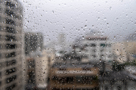 window glass with raindrops showing blurred city in the background, rainy dayの写真素材