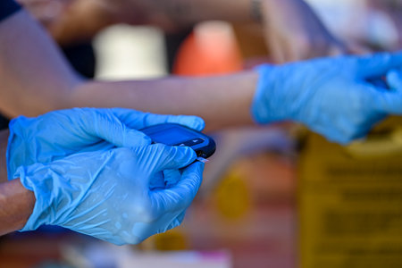 Nurse with a glucometer and patient ready to perform a blood glucose test. Sharps disposal container in the background.の写真素材