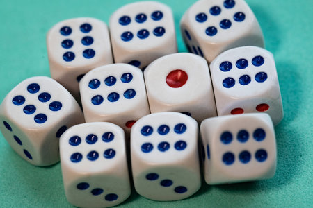 Close-up of a group of white dice with blue dots and a single red dot, arranged on a green surface. The composition emphasizes randomness and probability, often associated with gambling, games, and chance. The shallow depth of field highlights the dice in the foreground while gently blurring the background.の写真素材