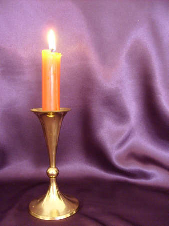 Lit red candle in brass candlestick against purple satin backdrop の写真素材