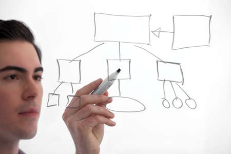 Young, handsome professional working on a flow diagram on on a see-through board on white background. Focus on flow diagram.の写真素材