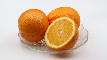 whole and cut oranges in a glass dish on a white background, close-up.