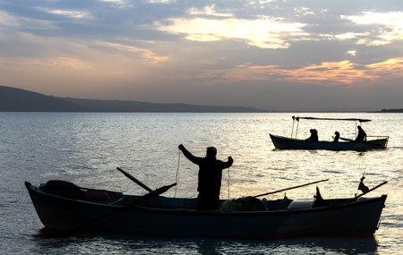 Silhouette of Fishermen on the boat in the lake at sunsetの写真素材