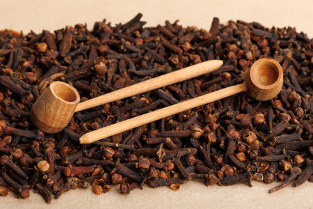 Heap of aromatic clove seeds with wooden spoons on light background