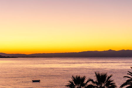 silhouette of a boat and sunset on the Agean sea with palm trees and boat in the foreground, from Edremit, BalÄ±kesirの写真素材