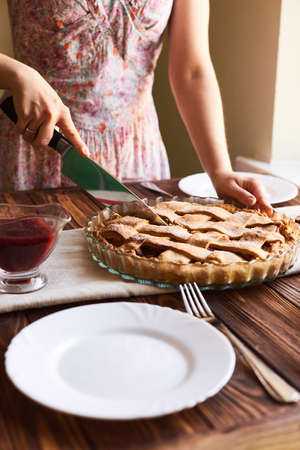 Woman putting delicious american pie on table. Close-up woman's hands cutting a homemade apple pie. White plates on the tableの写真素材