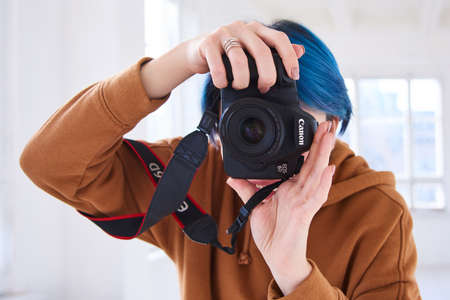 hipster girl holding canon 6d with 50 mm f/1.8 and taking photo. closeup of hand of young woman with professional camera in studio. world photography day conceptのeditorial素材