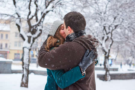 Young loving couple dressed in plaid scarves walk at the old city in winter. Hugging and kissingの写真素材