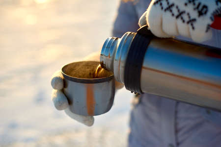 Hands  cups of tea and  flask in snowy winter close up viewの写真素材
