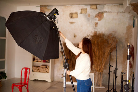 Concept of creative work in photo studio. woman setting photographing equipment getting ready for a photo shoot.の写真素材
