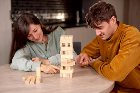 Happy couple playing wooden block game while sitting in kitchen at home, having fun togetherの写真素材