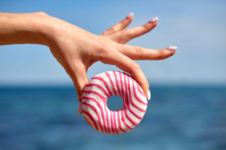 shallow depth of field donut in hand on blue sky and sea background. concept of sweet snack on...