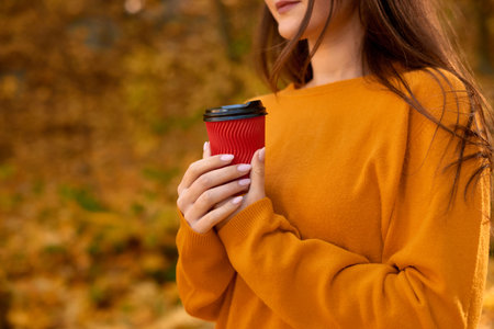 close up woman hands hold red paper cup on fallen yellow leaves backgroundの写真素材