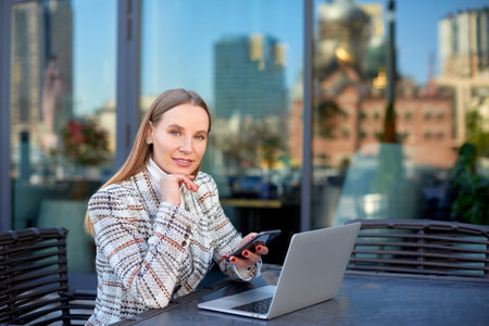 blonde caucasian woman freelancer is working with her project on laptop remotely from a city cafe outdoorsの写真素材