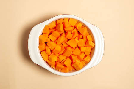 chopped pumpkin pieces in a saucepan top view. healthy food concept. Flat lay of utensils for cooking on beige backgroundの写真素材