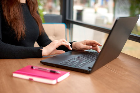 woman hands type text on keypad on laptop. Cropped view of office worker sitting at table in cafe