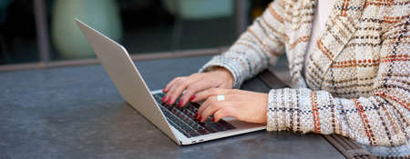 Cropped view of office worker sitting at table in cafe. Female hands type text on keypad on laptopの写真素材