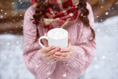 Young woman holding cup of hot chocolate with marshmallows outdoors in winter dayの写真素材