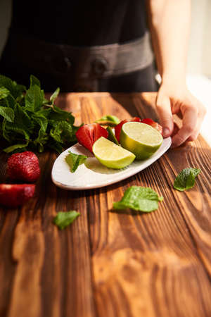 cooking of cooling summer cocktail with strawberries, ice and mint and around the berries are ripe fresh strawberries and limeの写真素材