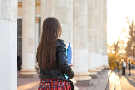 Female student back to camera. Woman holds folders in hands and goes to college. Learning offline, education conceptの写真素材