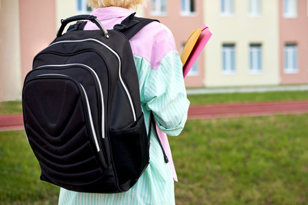 Student female with black backpack and folders for notebooks and books in hands go to school
