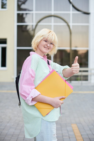 female student showing cool gesture and standing in front of university campusの写真素材