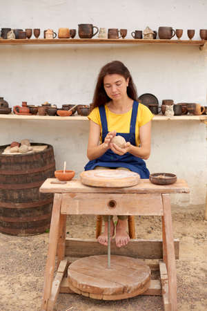 woman in blue apron and yellow T-shirt makes clay product on mechanical potters wheelの写真素材