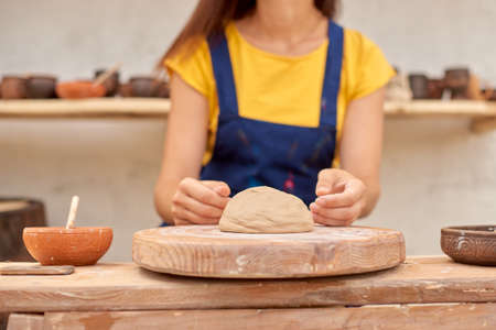 closeup woman hands in work on mechanical potter's wheel against background of shelves of clay productsの写真素材