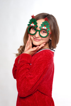 vertical Christmas portrait of cheerful girl in new year wear holds hands near face on white studio backgroundの写真素材