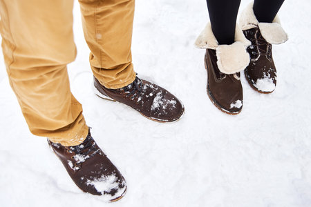 couple in love wear brown boots stay and walk on white fresh snow in winter. winter comfortable shoesの写真素材