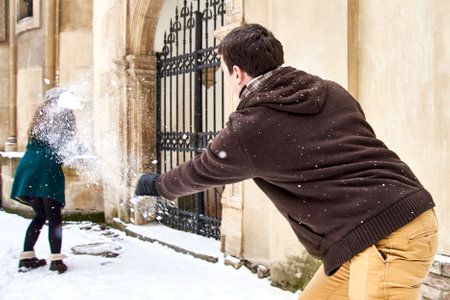 boy throws snowball in girl in yard. winter fun and entertainment outdoorsの写真素材
