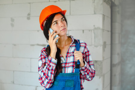 concentrated worker woman in blue overall having phone conversation during break from work at...