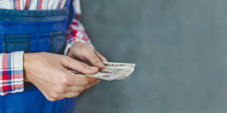 woman counts banknotes from bundle of money with denomination of 50 dollars on gray and blue...