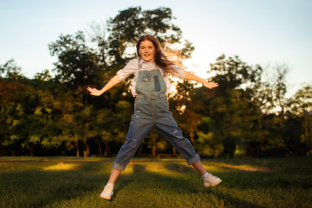 school girl jump and have fun on lawn with green trees backgroundの写真素材