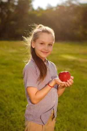 smiling girl child holding red fresh apple in green park. concept of healthy snack for children on walkの写真素材