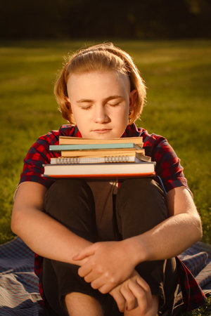 teenager boy studying in green park, sitting on green grass with stack of books. preparing to pass examsの写真素材