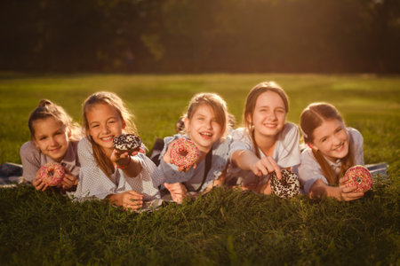 celebration of World Children's Day. Happy girls laying on green grass and eating sweet donuts in park. focus on hands, face in background out of focusの写真素材