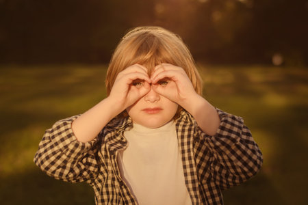 child boy in casual white t-shirt looking through gesture in binoculars, observing distant with attentive look, watching afar. Hands make binoculars and eyes look through themの写真素材