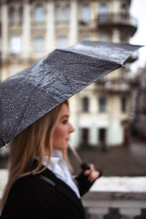 focus on rain drops on black big umbrella in woman hand. young business woman walking to meetingの写真素材