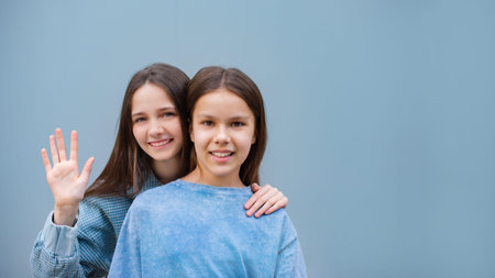 two cheerful teen girls hand on shoulder toothy smile look camera isolated on blue color backgroundの写真素材