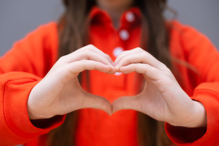 focus on shape of heart woman hands on red sweatshirt background