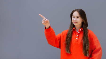teen girl in red sport sweatshirt pointing forefinger gesture on empty free place for text gray wall backgroundの写真素材